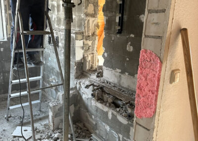 Handwerker, der mit einer Bohrmaschine in einem Innenraum an einer Wand arbeitet.