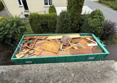 Grüner Container gefüllt mit Holzabfällen, darunter Bretter und Platten, auf einer Straße in Wickede.